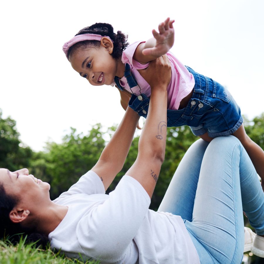 Black family, park and flying with a mother and daughter having fun together while bonding on grass.